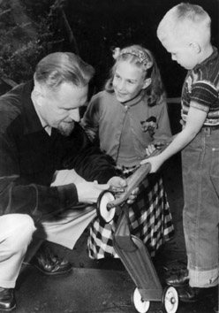 Dr. tenBroek repairs the children's scooter while Anna and Nick look on.